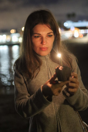 Young woman holding small candlelight by the water at nightの写真素材