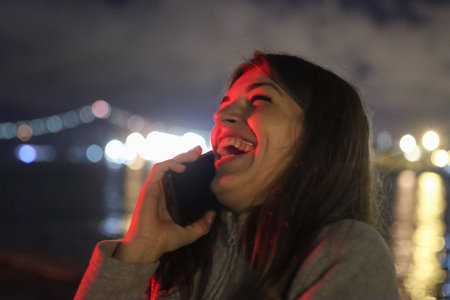 Joyful young woman laughing on smartphone at nightの写真素材