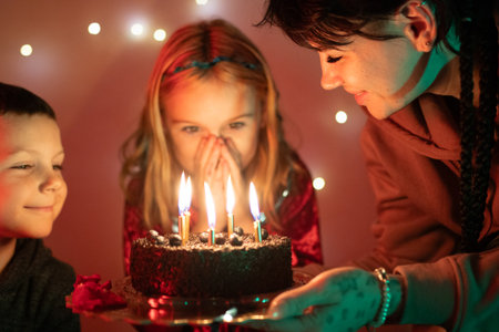 Children celebrating birthday, watching lit candles on cake