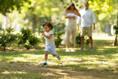 Toddler boy running happily in sunny park with parentsの写真素材