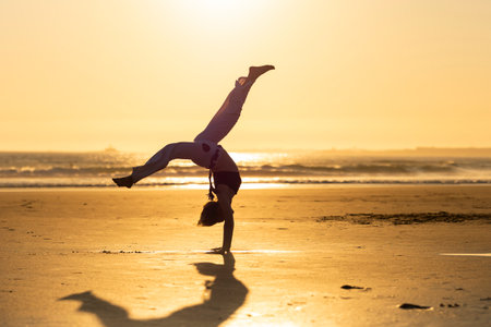Capoeira student performing a cartwheel on beach at sunsetの写真素材