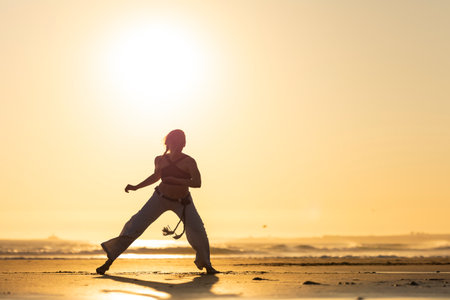 Person doing capoeira martial art on beach at sunsetの写真素材