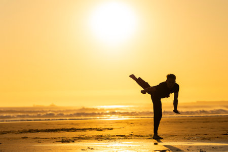 Man practicing martial art kick on beach at sunsetの写真素材