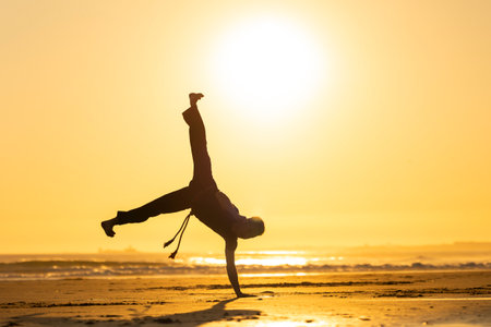 Man performing capoeira handstand on beach at sunsetの写真素材