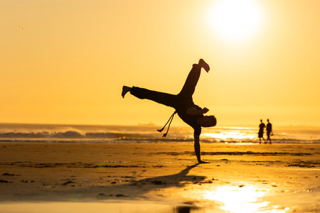 Performer balancing handstand capoeira movement on beach at sunsetの写真素材