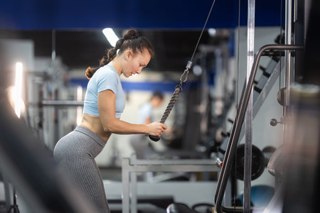 Woman exercising triceps with rope pull machine in gym