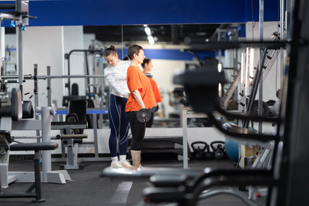 Personal trainer guiding woman lifting dumbbell in gym