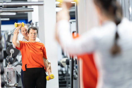 Senior woman exercising with personal trainer in gym