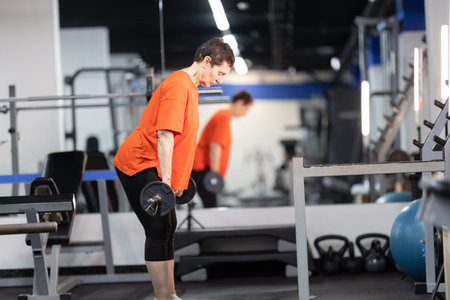 Senior woman performing strength training with barbell in gym