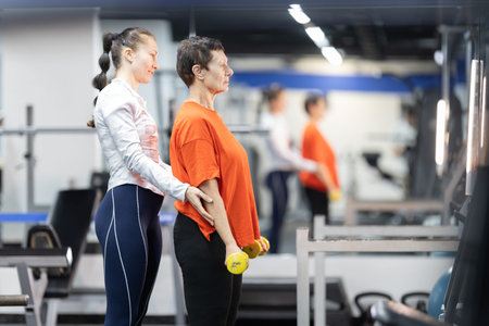 Personal trainer guiding senior woman lifting dumbbells