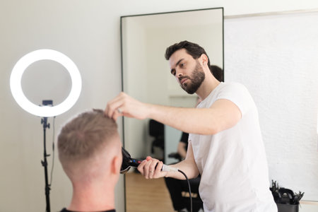 Professional male barber styling clients hair with hairdryer
