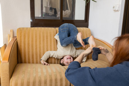 Child having fun on couch getting dressed by adult