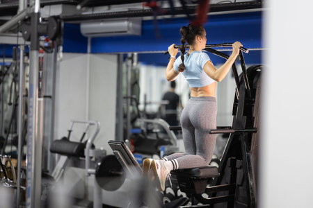 Woman exercising on pull-up machine in fitness gym