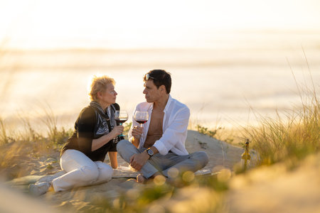 Senior couple enjoying romantic sunset wine on beachの写真素材