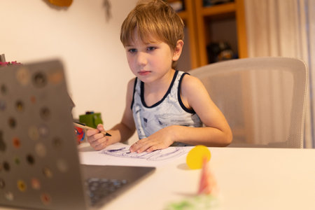 Young boy learning online and drawing at home desk