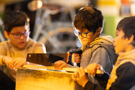 Boys learning woodworking using saw in workshop