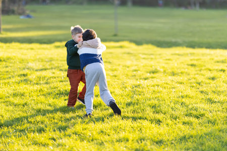 Little boys playing fighting game in sunny green park