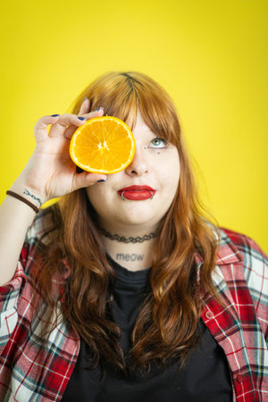 Young woman covering eye with vibrant orange slice