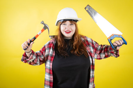 Woman wearing hard hat holding hammer and saw