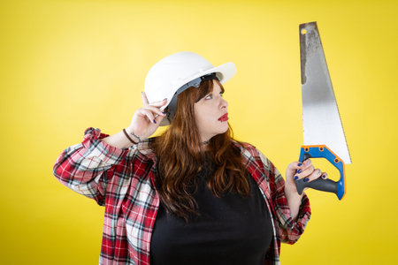 Woman wearing hard hat holding hand saw looking right