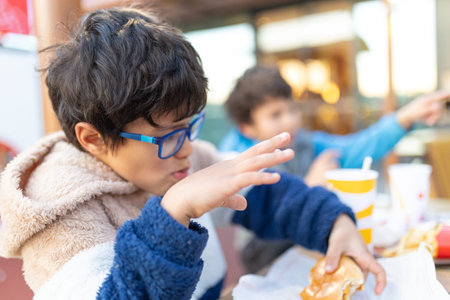 Young boy eating fast food burger with friendの写真素材