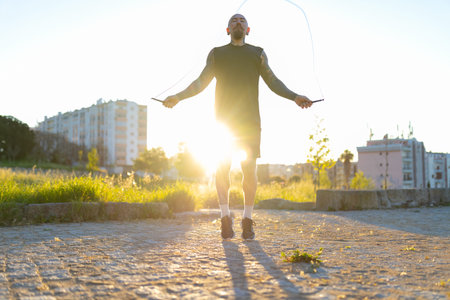 Athletic man skipping rope under golden sun in park