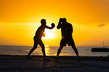 Couple boxing training outdoors at golden sunset by ocean