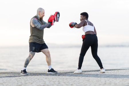 Coach training woman boxer striking focus mitts outdoors