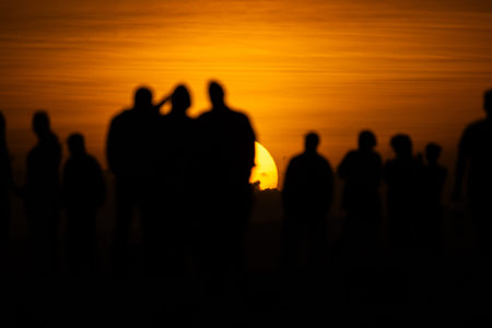 Group of people standing together during sunset at a scenic location with bright orange sky in the background