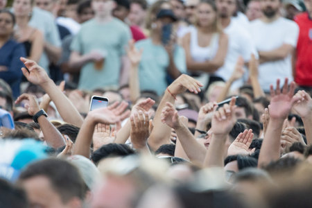 Crowd with raised hands during event at outdoor location on sunny day