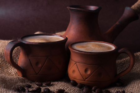 Coffee, morning, coffee beans concept - coffe in earthenware cup and coffe beans on brown backgroundの写真素材