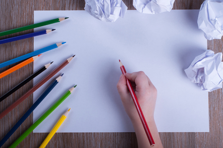 Colored pencils on white paper back to school concept - Child's hand preparing to write on a white sheet of paper with pencils and draftsの写真素材