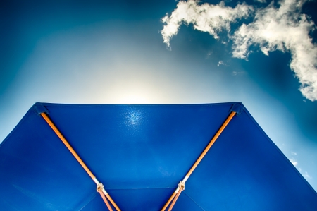 Detail of a blue sunshade in backlight against a blue sky with clouds の写真素材