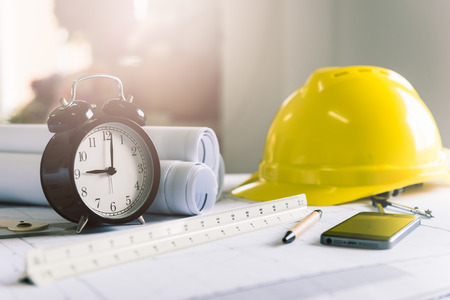 Morning time it's nine o'clock already, A retro clock showing 9:00 am on the desk of engineer designer and architect in an office with equipment and drawing paper for working plan.の写真素材