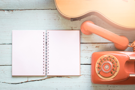 The diary blanks with retro telephone and acoustic guitar on the wooden table of music composer for musical notes.の写真素材