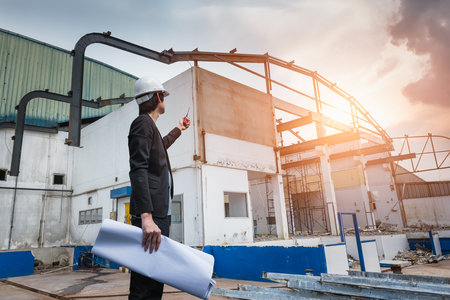 Civil engineer checking work and the holding drawing paper with walkie-talkie for communication to management team in the construction siteの写真素材