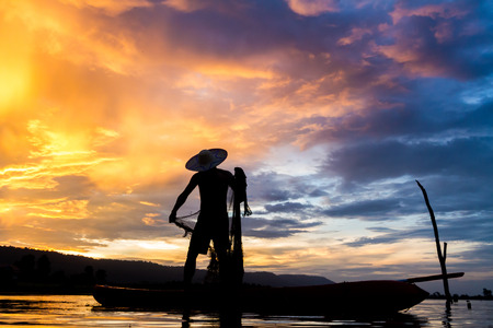 Silhouette of asia fisherman in action when fishing at sunsetの写真素材