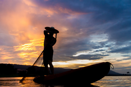 Silhouette of asia fisherman in action when fishing at sunsetの写真素材