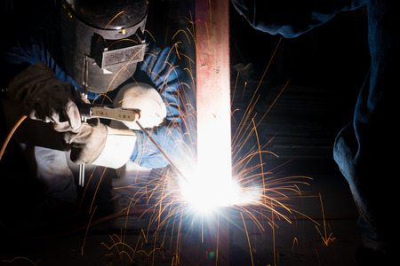Welding skills training of welder with protective mask and welding steel metal part.