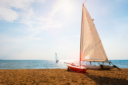 Sailboat on beach and sky background with windsurfing in the wind through the waves at the sea., International Laser Class sailboat, also called Laser Standard and the Laser One on beachの素材 [FY310123218092]