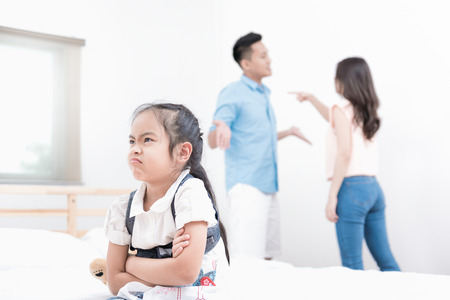 Attractive little girl is looking unhappy while sitting on the bed at home and angry away crossed her arms hands, sad against arguing parents at home or Conflict happened in the familyの写真素材