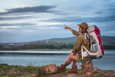 Young Woman Hiker with backpack sits enjoying the view of mountain peak and lake in evening, Camping at night in travel activity conceptの写真素材