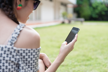 Asian girl sitting and using cellphones in the garden. Social network service concept.の写真素材