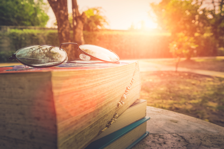 Close up glasses and book on table in garden with sunrise for background.の写真素材
