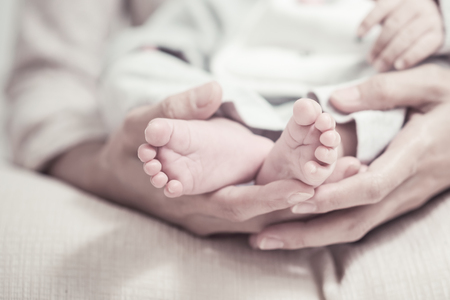 Feet of the newborn baby in parents hands. Moment of mother's care after maternity concept. Selection focuses to toe and add vintage color filter for feeling image.の写真素材