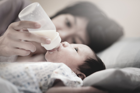 Asian Newborn Baby's drinking milk from bottle holding by mom. Mother's care concept and healthy lifestyle. Selection to baby eyes feeling. Vintage style color filter.の写真素材