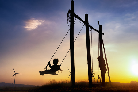 Silhouettes of happiness life of child to playing swing in turbine wind park renewable on sunset. Family Responsibility, Corporate Social Responsibility and sustainable energy concept.の写真素材