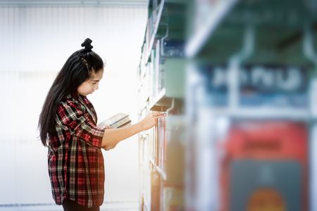 Asian Student searching for textbook in the bookshelf in the International College/University Library. Finding the correct answer to their question preparing for university examination.の写真素材