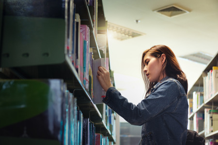 Asian Student searching for textbook in the bookshelf in the International College/University Library. Finding the correct answer to their question preparing for university examination.の写真素材