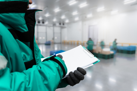 Hand of worker with clipboard checking goods in freezing room or warehouse. Export-Import Logistics...